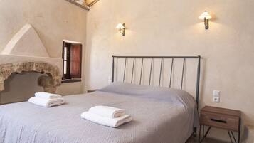 A bedroom with a large bed, a wooden nightstand, and a stone archway.