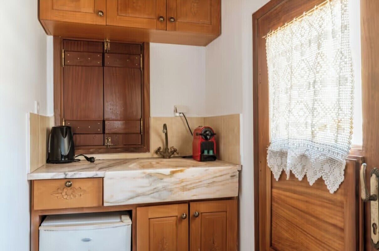 Una cocina compacta con armarios de madera, encimera de mármol, cafetera y electrodoméstico rojo.