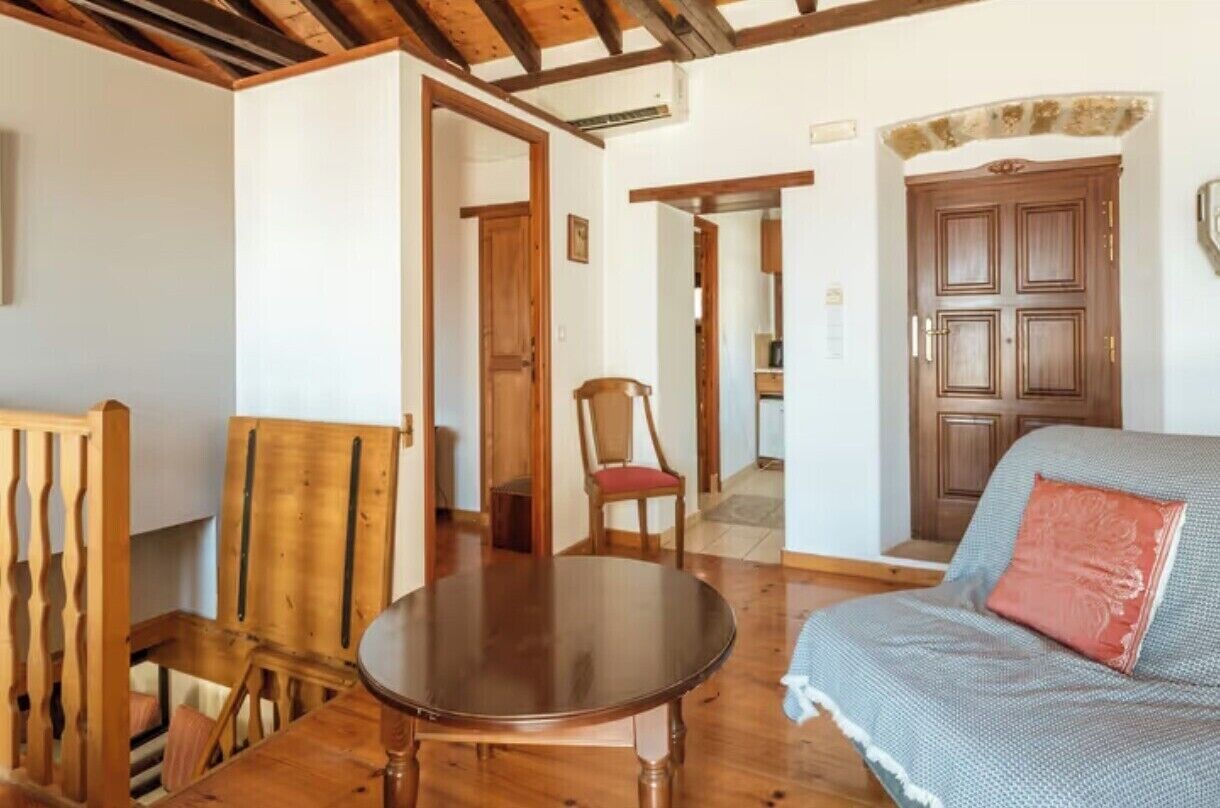 A cozy room with a wooden dining table, a sofa with a patterned throw, and a wooden door.