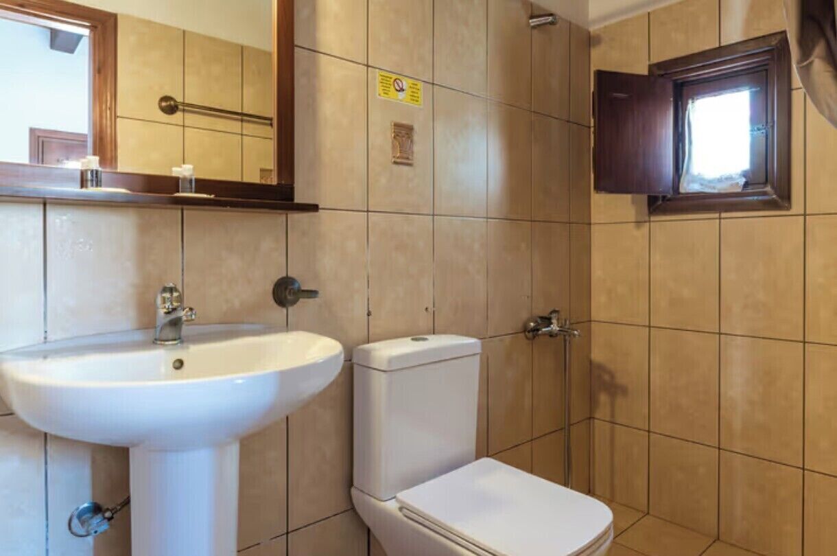 A bathroom with a white sink, toilet, and a window with a wooden frame.