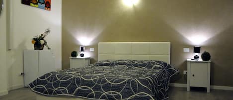 A bedroom with a bed, two bedside tables, a nightstand, a wall-mounted light, and a small potted plant.