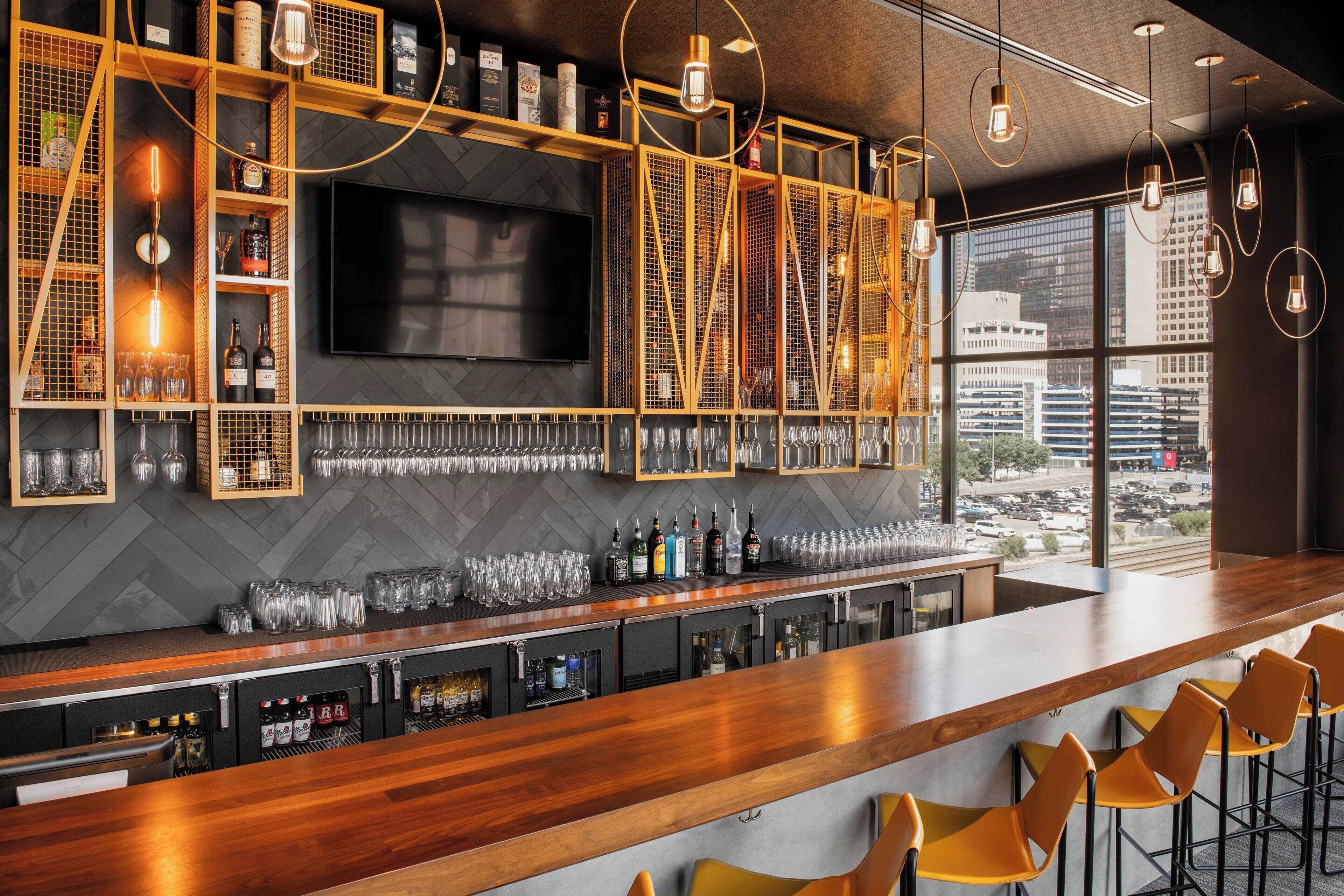 A bar area with a herringbone-patterned wall, a flat-screen TV, and a city view through large windows.