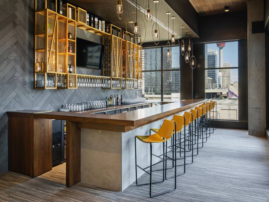 A modern bar area with a long counter, multiple stools, and a herringbone-patterned wall.