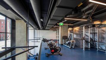 Un gimnasio con equipo de ejercicio, un pilar de hormigón y una ventana con vistas a edificios.
