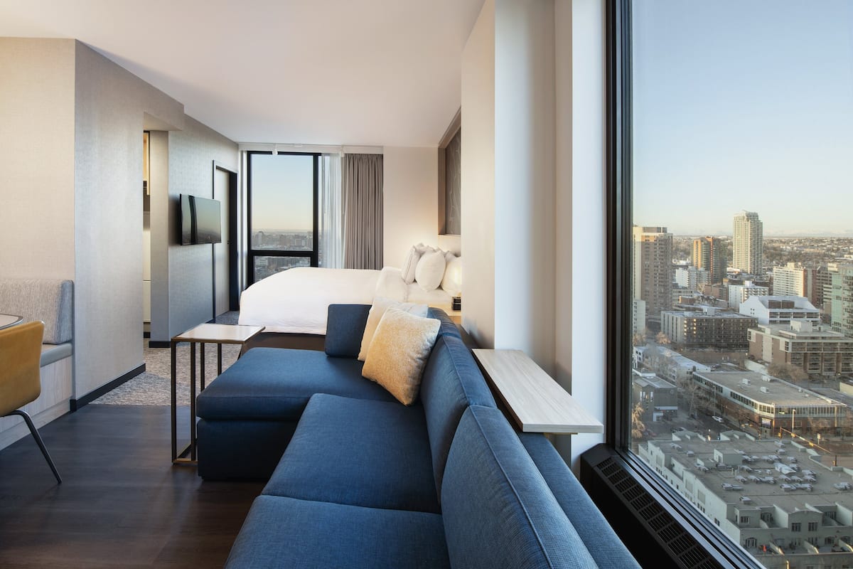 A modern hotel room with a large bed, a sofa, a desk, and a city view.