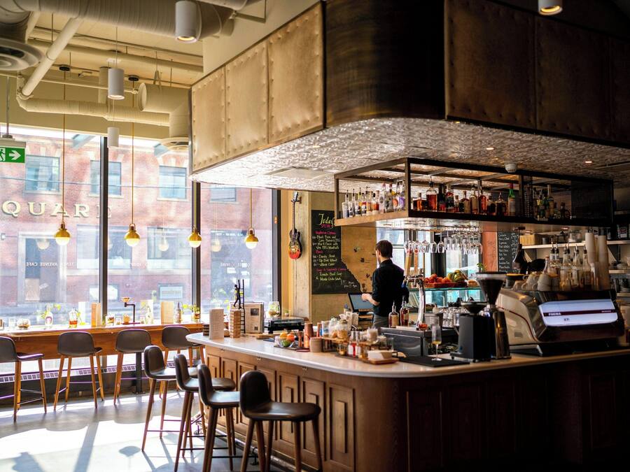 A bar area with stools, a bar counter, and a person working behind the counter.