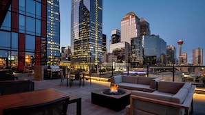 Eine Dachterrasse mit Sitzgelegenheiten im Freien, einer Feuerstelle und Blick auf die Stadt.