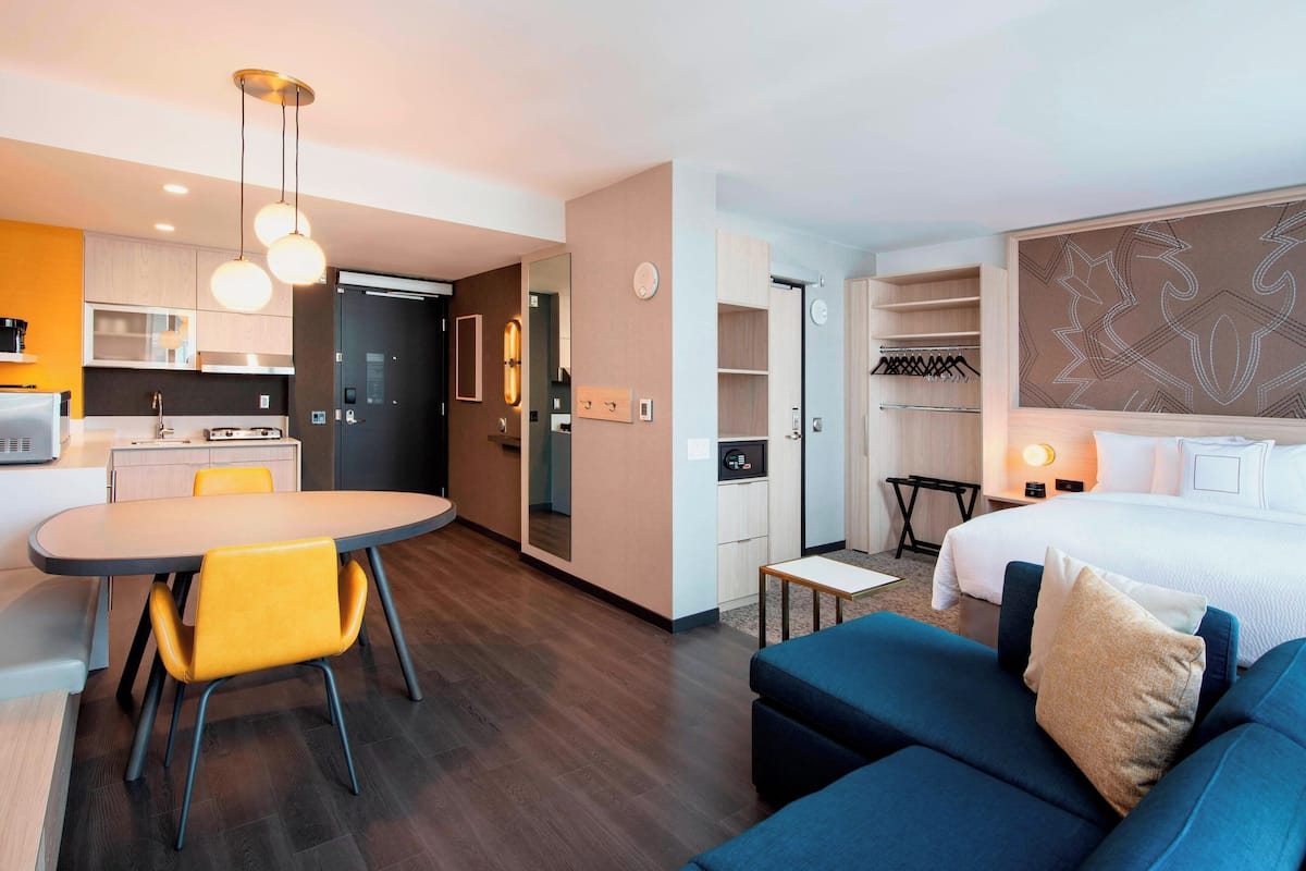 A modern hotel room with a dining area, a sofa, a bed, and a walk-in closet.