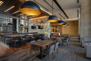 A modern restaurant with wooden tables and chairs, large pendant lights, and a mural on the wall. - Residence Inn by Marriott Calgary Downtown/Beltline District (Calgary)