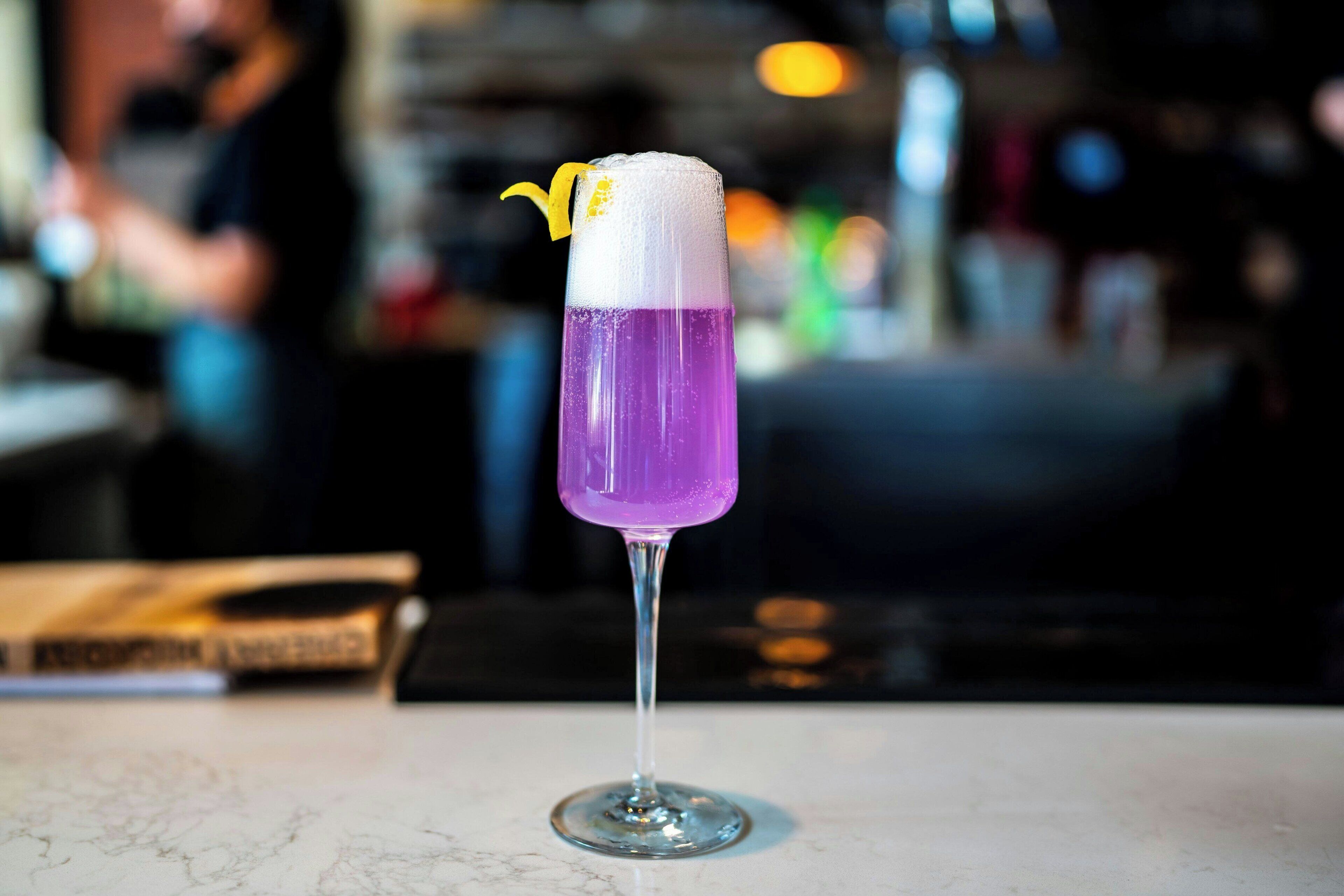 Un cóctel morado en un vaso con un adorno amarillo, sobre una superficie de mármol.