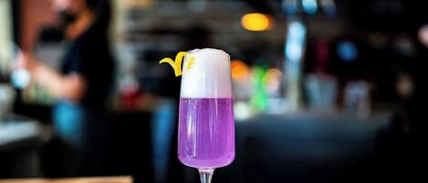 Un cóctel morado en un vaso con un adorno amarillo, sobre una superficie de mármol.
