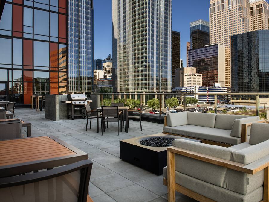 Una terraza en la azotea con mobiliario exterior, una chimenea y vistas a un paisaje urbano con edificios altos.