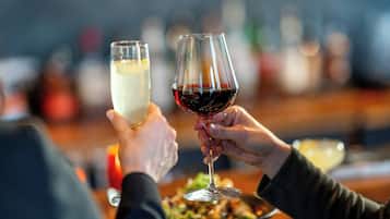 Dos manos sosteniendo copas de vino, una con vino blanco y la otra con vino tinto, en un bar con fondo desenfocado.