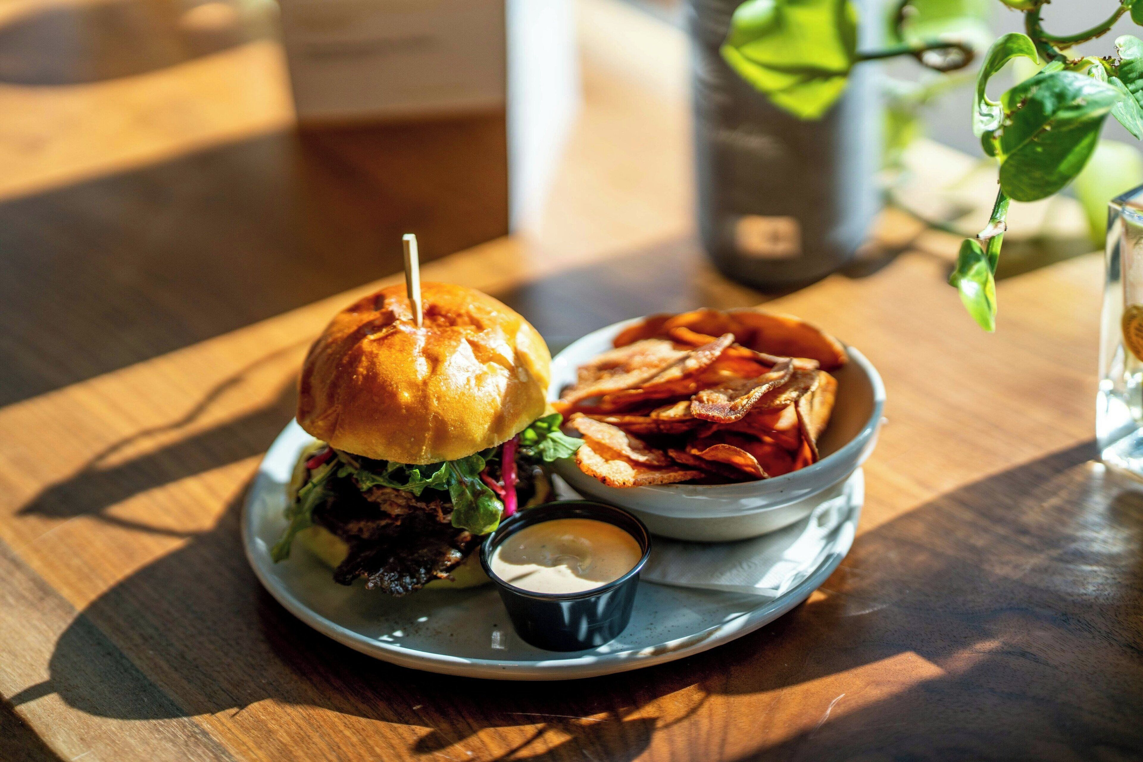 A meal consisting of a burger, fries, and a small cup of sauce on a plate.