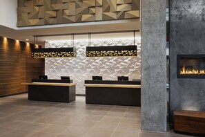 A modern reception area with two reception desks, a textured wall, and a fireplace. - Residence Inn by Marriott Calgary Downtown/Beltline District (Calgary)