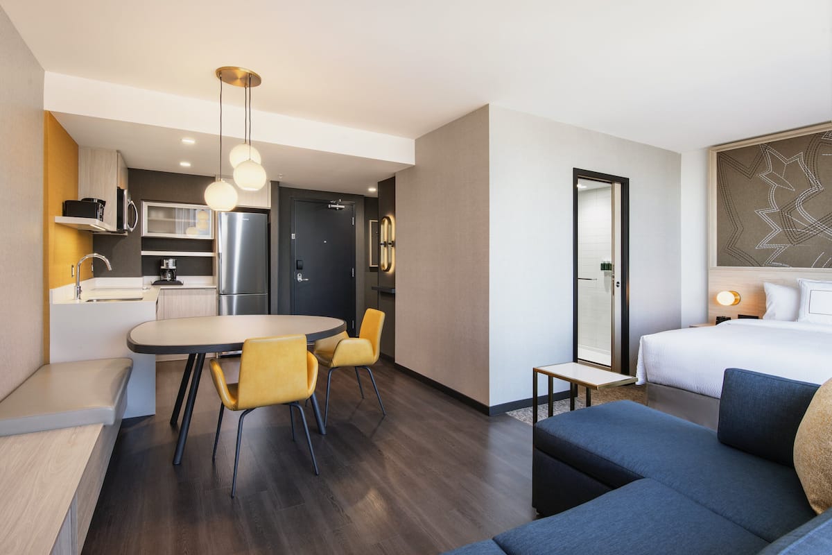 A compact hotel room with a kitchenette, a dining area, and a bed.