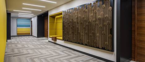 A modern hallway with a patterned carpet, a yellow seating area, and a decorative wall panel.