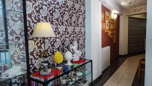 A hallway with patterned wallpaper, a glass display case with various items, and a lamp. - Hotel Miramonti (Gangi)