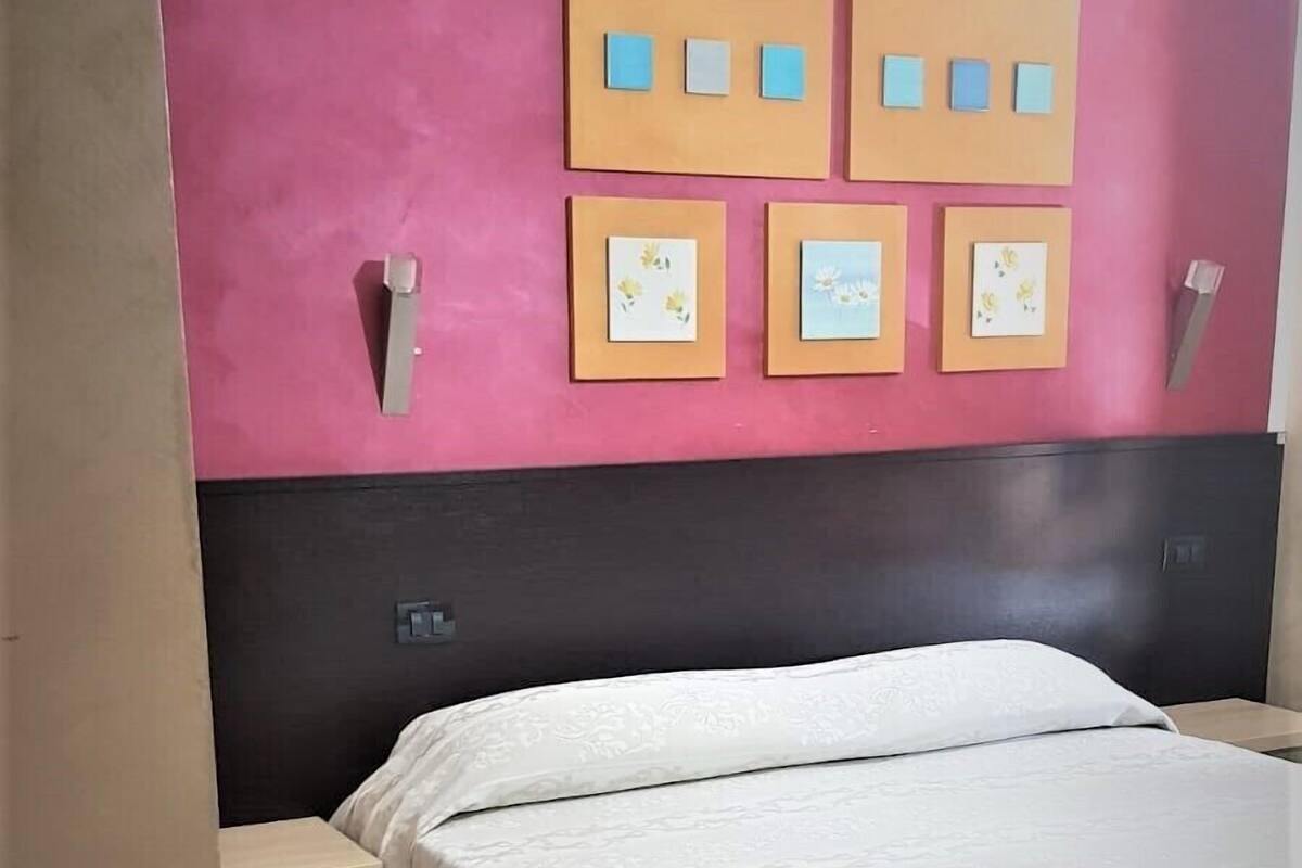 Quarto com cama, mesa de cabeceira e prateleira com molduras.