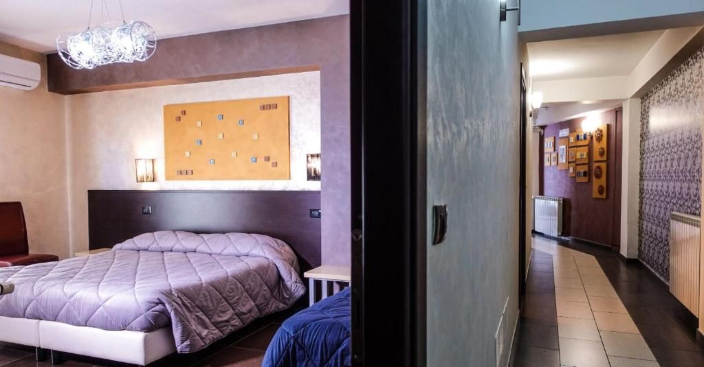 A hotel room with a bed, a wall-mounted artwork, and a hallway with a patterned wall and a radiator.