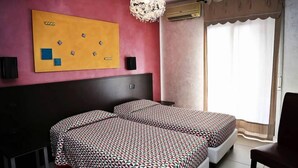 A hotel room with two beds, a large yellow artwork on the wall, a chandelier, and a window with curtains. - Hotel Miramonti (Gangi)