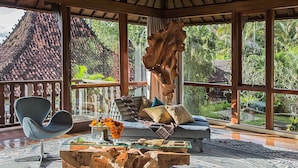 Una habitación amplia con un gran ventanal, techo de madera, un sofá, una silla y una mesa de centro con un jarrón de flores.
