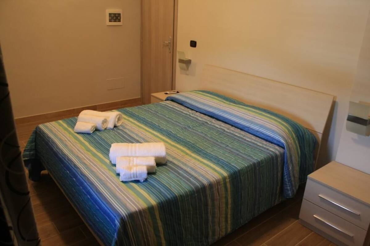 Une chambre d’hôtel avec un lit, une table de chevet et une lampe fixée au mur.