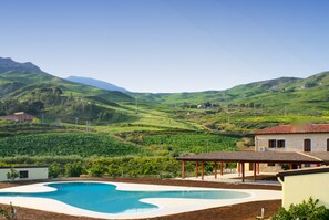 A swimming pool with a curved edge, surrounded by a building with a tiled roof and a covered area.