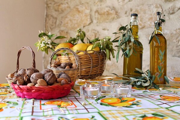 A table with a fruit basket, candles, and olive oil bottles.