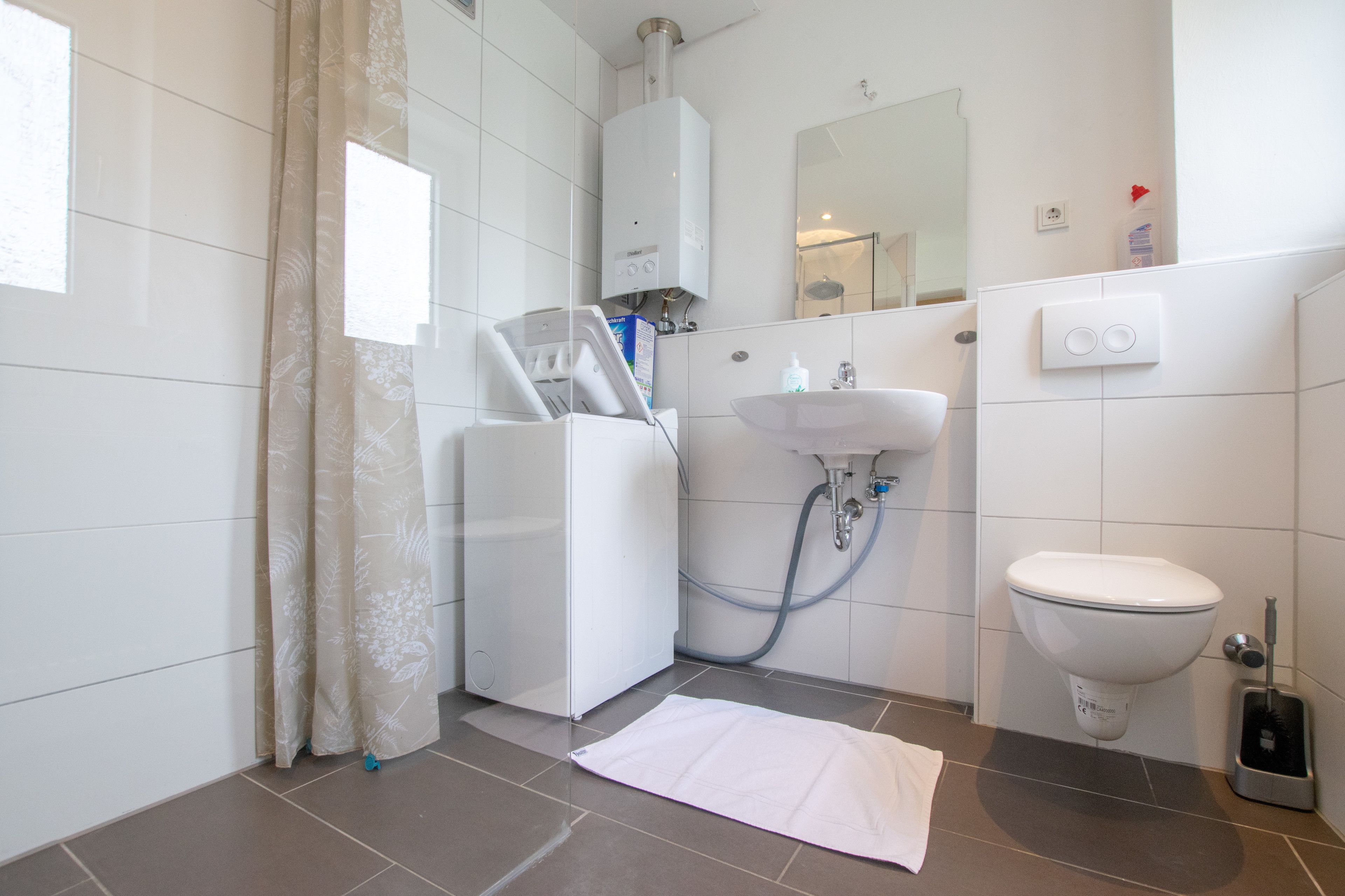 A modern bathroom with a white toilet, a sink, a shower, and a towel on the floor.