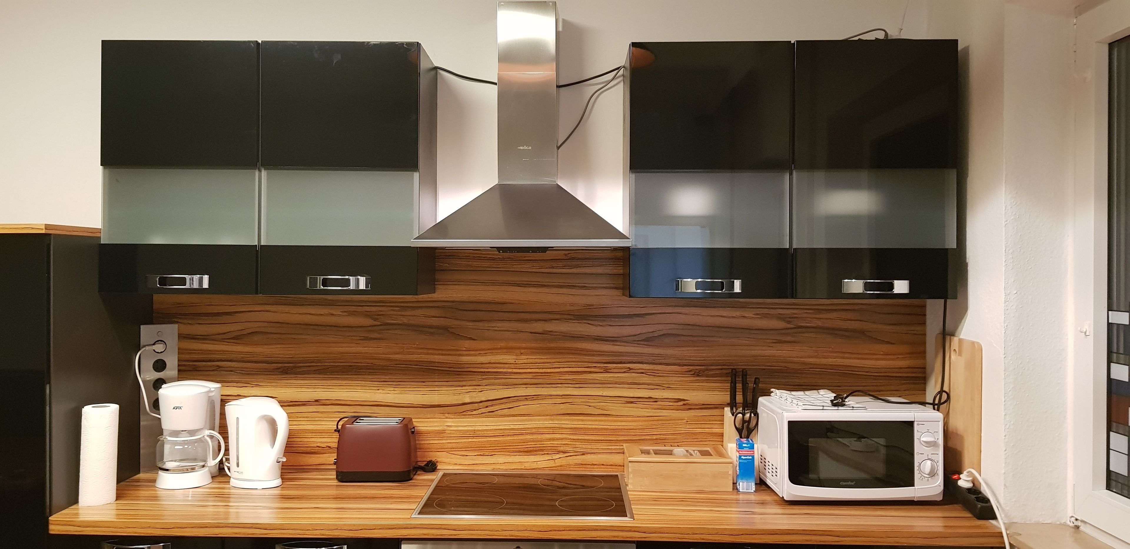 A kitchen with dark cabinets, a wooden countertop, a coffee maker, a toaster, and a microwave.