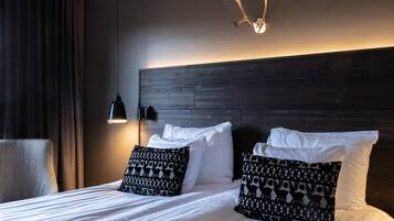 A neatly made bed with white linens and patterned pillows, a dark wooden headboard, a wall-mounted light fixture, and a curtain to the left.