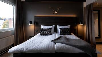 Habitación de hotel moderna con una cama grande, dos lámparas de noche, un adorno de asta de ciervo en la pared y vistas de la ciudad a través de la ventana.