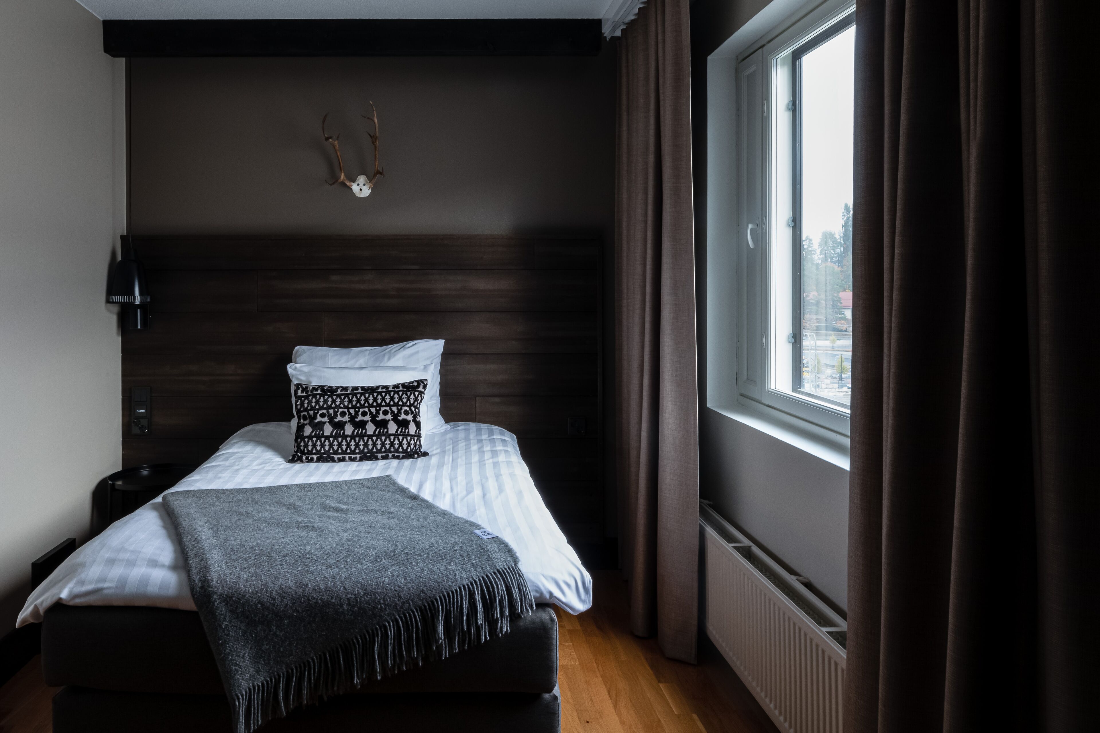 Ein Schlafzimmer mit Bett, Kopfteil, Fenster mit Vorhängen, einer Wandlampe und einer Wanddekoration.