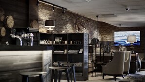 A bar area with stools, a seating area with chairs, a television screen, and a brick wall with a clock. - Lapland Hotels Kuopio (Kuopio)