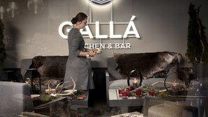 A person serving food at a table with antlers and a candle, in a restaurant named "CALLÁ CHEN & BAR" with a modern interior and a logo on the wall. - Lapland Hotels Kuopio (Kuopio)