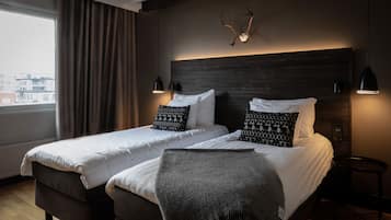 A hotel room with two beds, a large window with curtains, a wooden headboard, and a mounted antler decoration.
