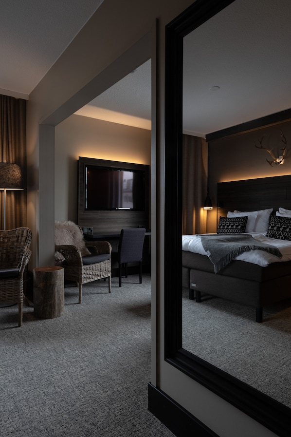 A modern hotel room with a large bed, a flat-screen TV mounted on the wall, a comfortable seating area with a chair and a small table, and a large mirror reflecting the room. - Lapland Hotels Kuopio (Kuopio)