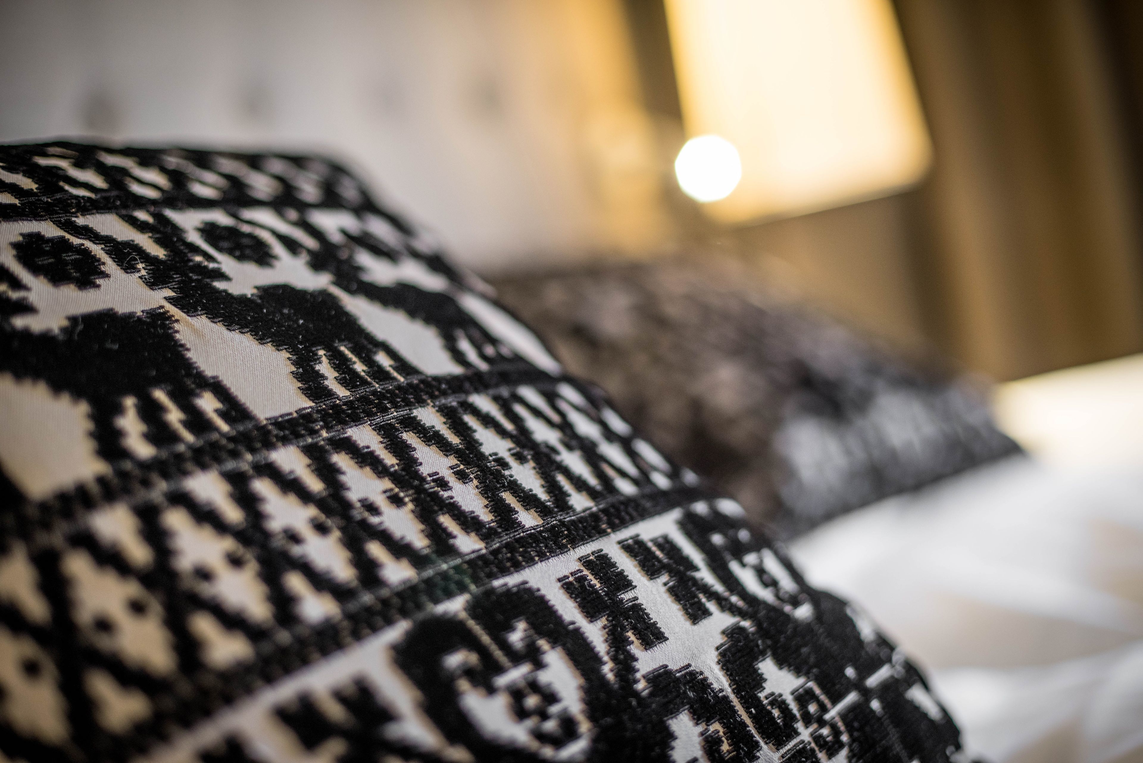 A close-up of a patterned pillow with a geometric design, placed on a bed in a hotel room.