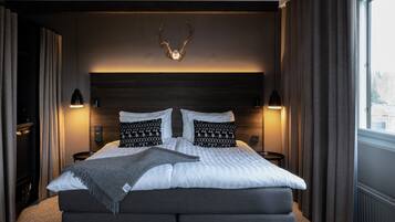 A bedroom with a large bed, two bedside lamps, a headboard with antlers, and a window with curtains.