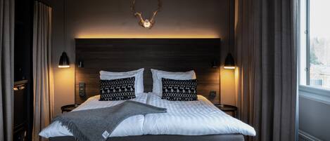 Un dormitorio con una cama grande, dos lámparas de noche, cabecera con cuernos y una ventana con cortinas.