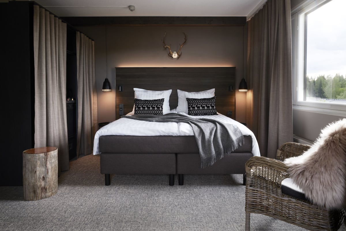 A modern bedroom with a large bed, a headboard with antlers, two bedside lamps, and a view of the outdoors through a window.