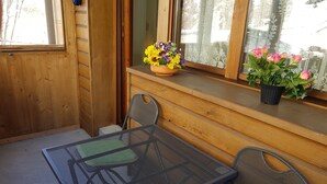 Eine Holzhütte mit einer kleinen Terrasse, auf der ein Metalltisch und zwei Stühle stehen.