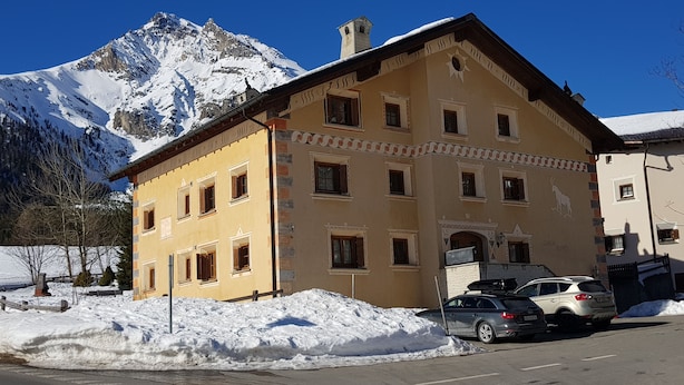 Ein gelbes Gebäude mit vielen Fenstern und einem schneebedeckten Berg im Hintergrund.