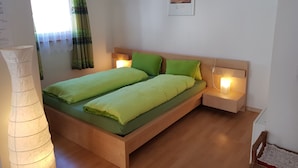 Ein modernes Schlafzimmer mit einem hölzernen Bett, grüner Bettwäsche, zwei Nachttischlampen und einem gerahmten Kunstwerk an der Wand.