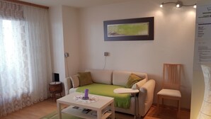 Ein Wohnzimmer mit einer Couch, einem kleinen Tisch, einem Sessel, einer grünen Decke und einem gerahmten Bild an der Wand.