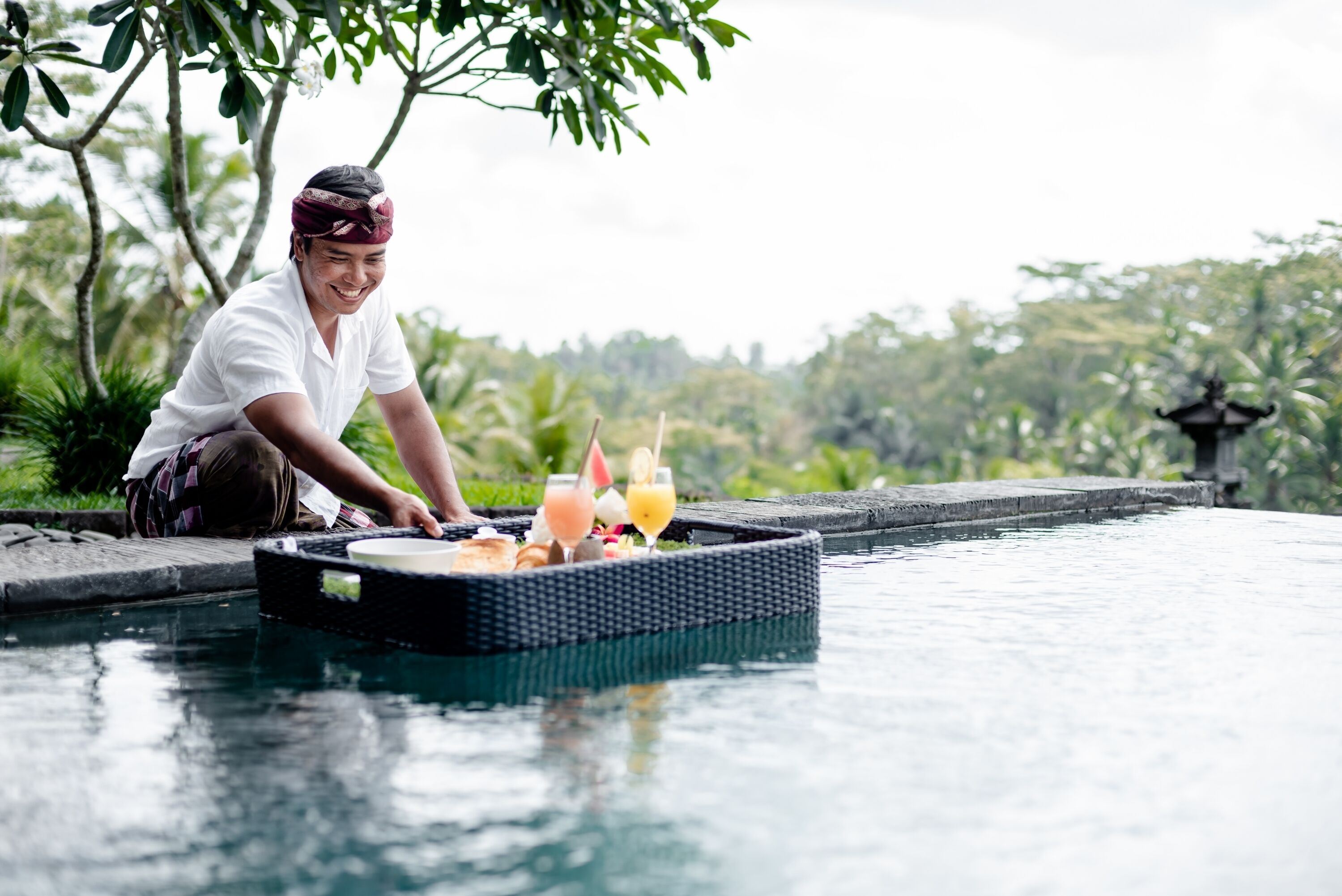 A person serving drinks from a floating tray over a pool.