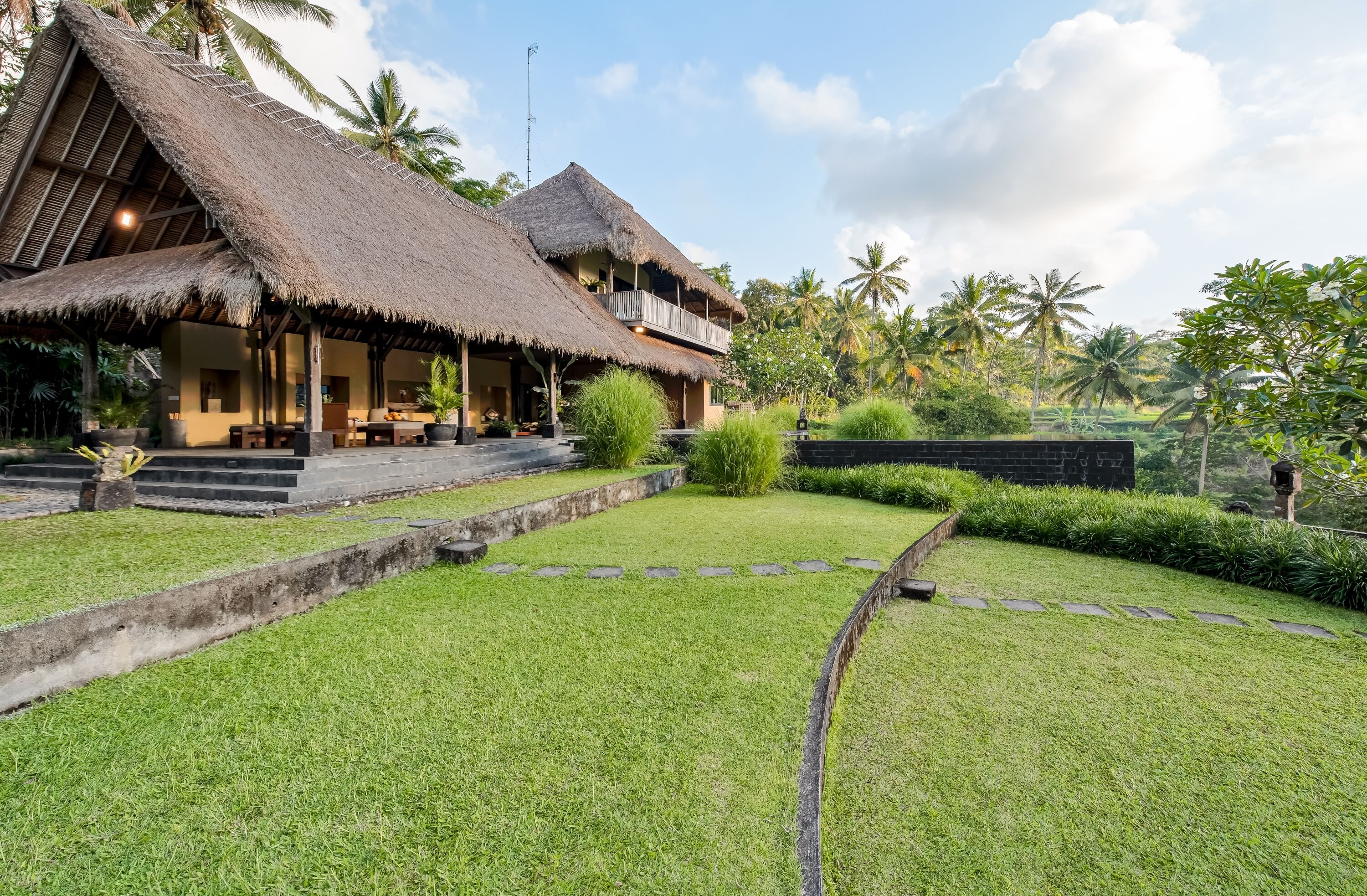 A bungalow with a thatched roof, a covered outdoor seating area, and a well-maintained garden with a stone pathway.