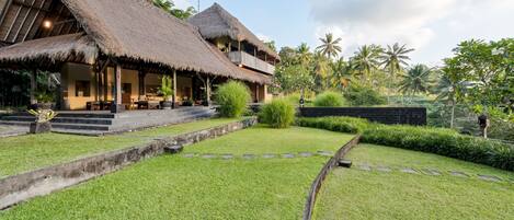 A bungalow with a thatched roof, a covered outdoor seating area, and a well-maintained garden with a stone pathway.