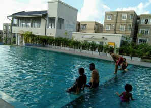 A swimming pool with people in the water, surrounded by buildings and greenery. - Srilanka Budget Apartment (Homagama)